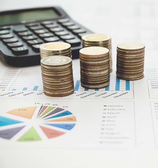 A stack of coins, a calculator and investment returns graphs shown in a office. 