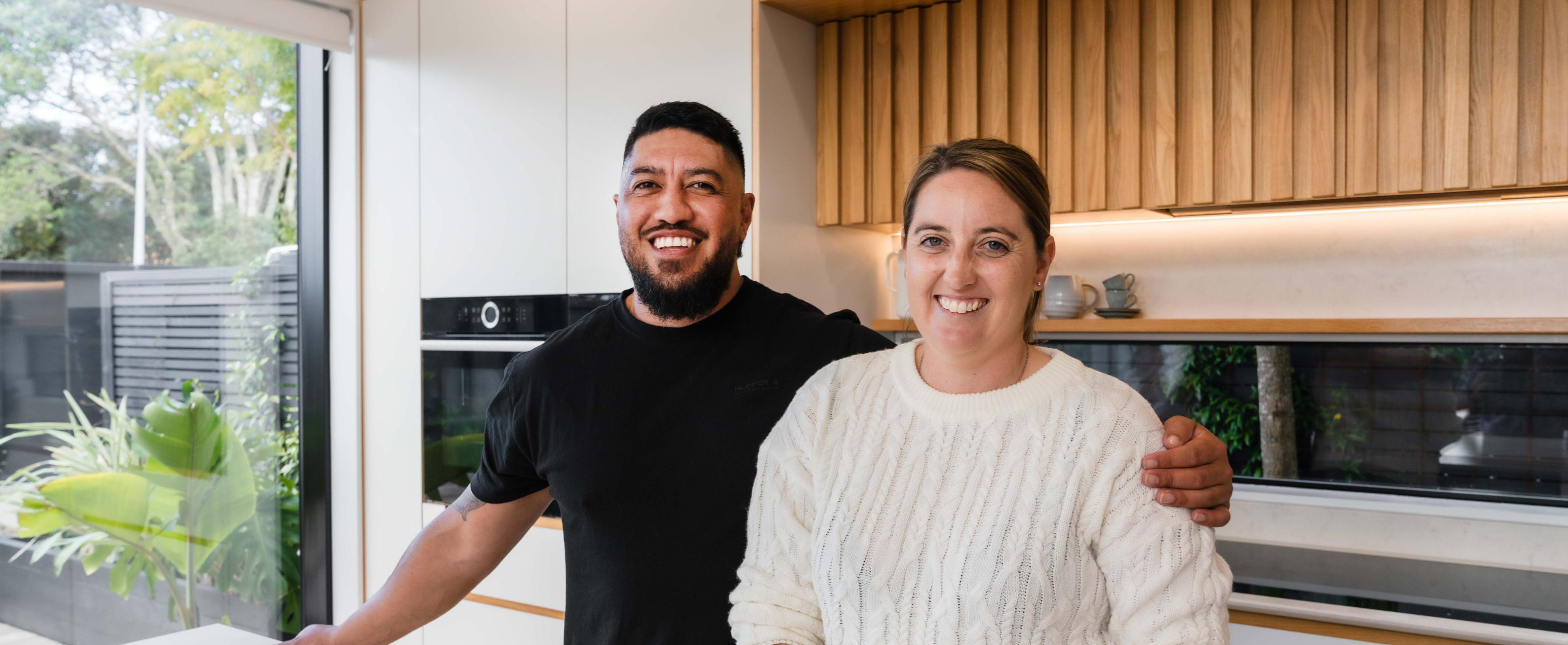 Young happy male/female couple in casual clothing smiling in a modern kitchen, happy to be with Generate KiwiSaver Scheme