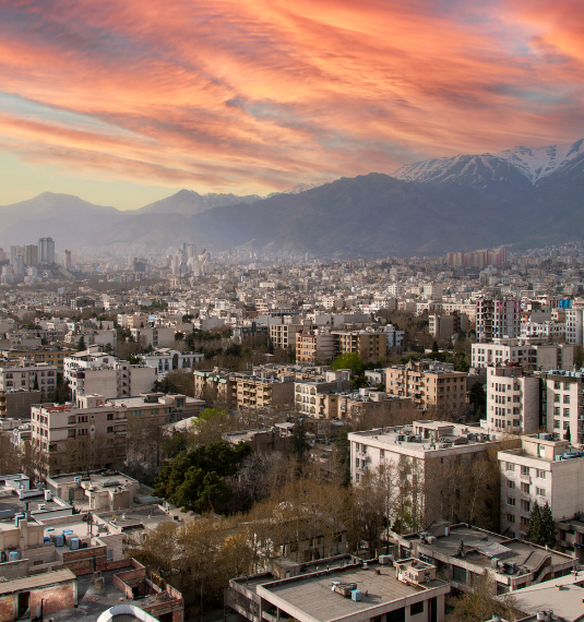The city of Tehran shown against a backdrop of mountains and red skies to represent the current conflict in Iran, the Middle East, US foreign policy, Trump, economic policy and the effects on global markets