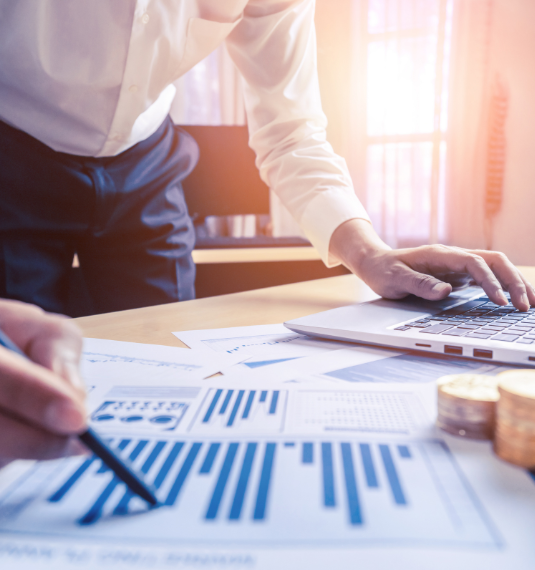 Photo of man's hands on a laptop and pointing to a bar graph near a pile of coins to represent DIY investing versus managed funds | Generate
