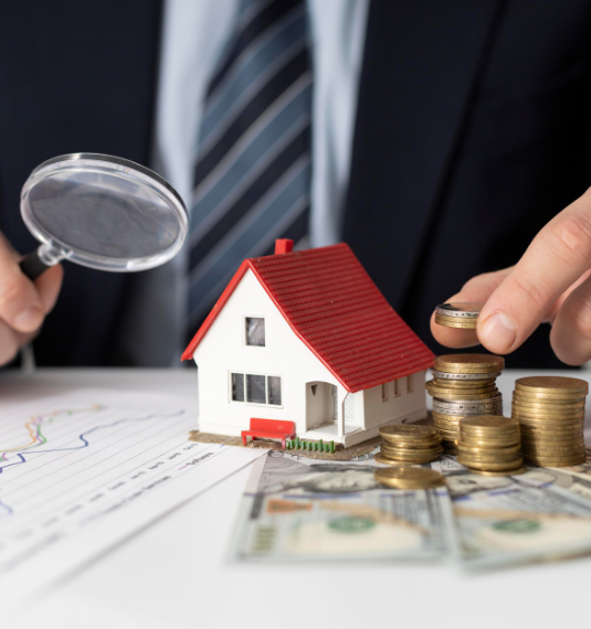 Photo of a man holding a magnifying glass looking at a toy house and a stack of notes and coins to represent the New Zealand housing market, property investors, rental yeilds and managed funds.
