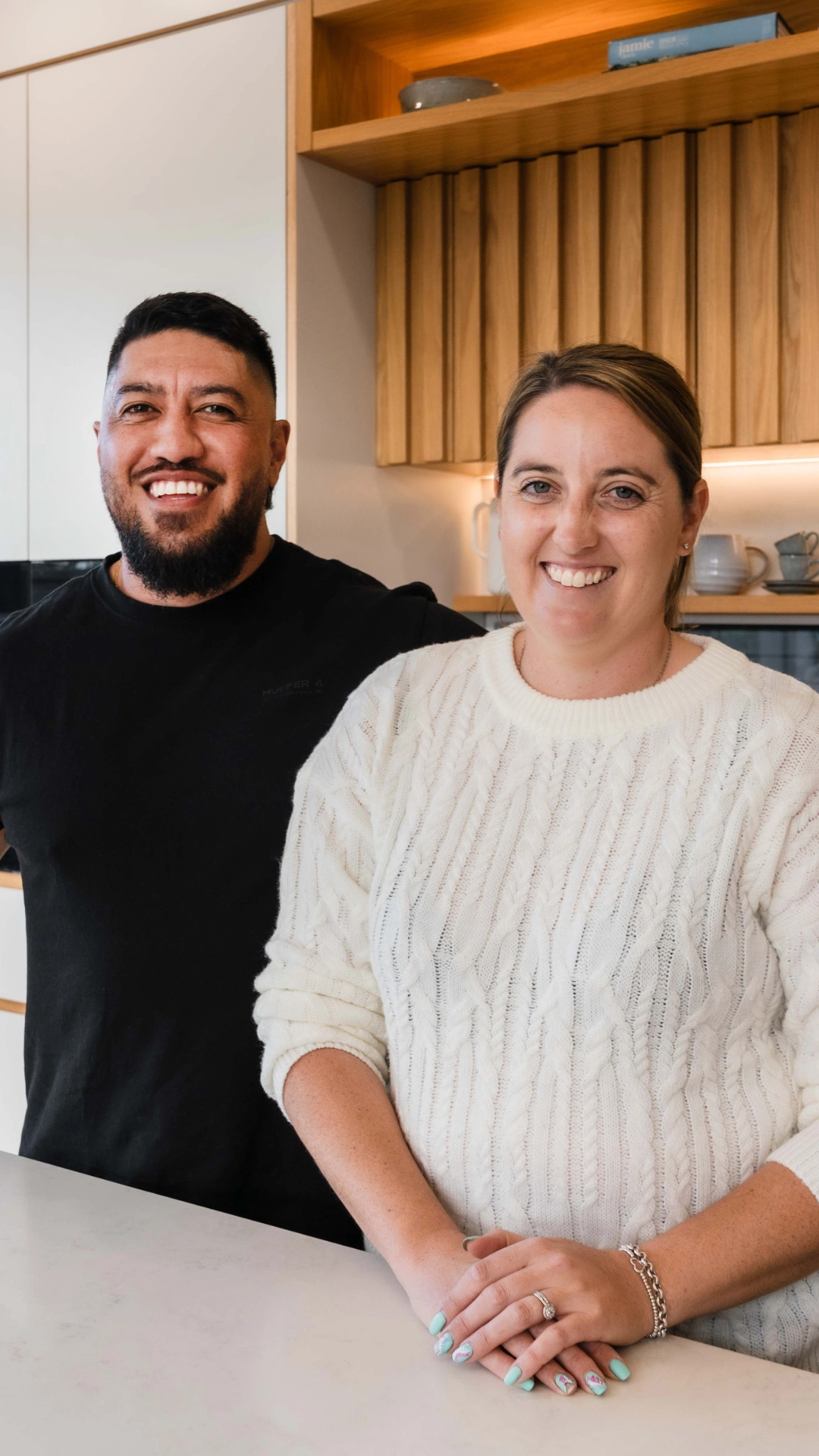 Young happy male/female couple in casual clothing smiling in a modern kitchen, happy to be with Generate KiwiSaver Scheme