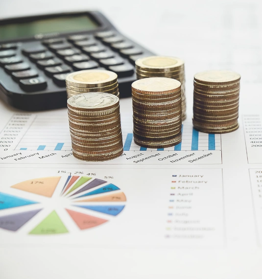 A stack of coins, a calculator and investment returns graphs shown in a office. 