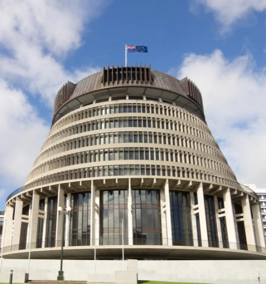Photo of NZ parliament building (the "beehive") with an NZ flag to represent the possible changes to KiwiSaver in the budget, government spending and KiwiSaver policy