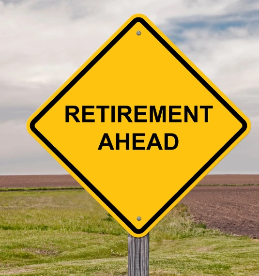A yellow road sign with the word "retirement" on it, with a green field and soil behind it to represent the issue of retirement for New Zealanders, KiwiSaver policy, superannuation and financial wellbeing