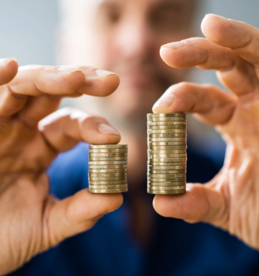 A man holding a small and large pile of coins in each hand to represent new Deloitte research has found KiwiSaver's median fees are now slightly lower than Australia's, despite the Australian superannuation system being around 35 times larger, reinforcing KiwiSaver's competitiveness on cost.