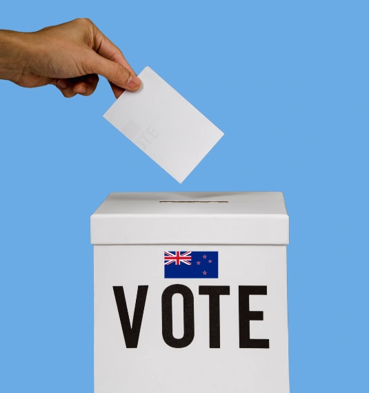Photo of a hand putting a ballot into a box to represent different KiwiSaver policies from National, Labour, ACT, NZ First and TOP